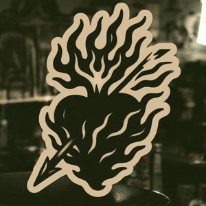 May include: A black and white illustration of a heart pierced by an arrow and engulfed in flames. The heart is stylized with a pointed bottom and a rounded top. The flames are stylized with sharp points and a swirling pattern.