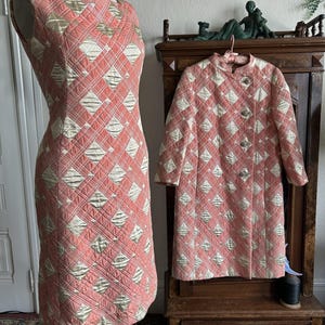 May include: A sleeveless dress and a matching long-sleeve coat featuring a quilted diamond pattern in coral pink and metallic gold. The coat has a high collar and a front button closure. Both garments display a consistent geometric design.