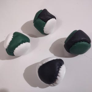May include: A set of four juggling balls crafted from textured leather panels in black, forest green, and white. Each ball features a multi-paneled construction with stitched seams, showcasing a rounded shape designed for tossing and catching.