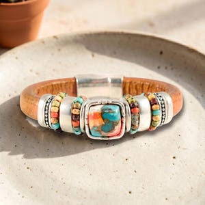 May include: A brown leather bracelet with a silver clasp and decorative silver accents. The bracelet features a square turquoise stone with orange and red hues, and colorful beaded sections.