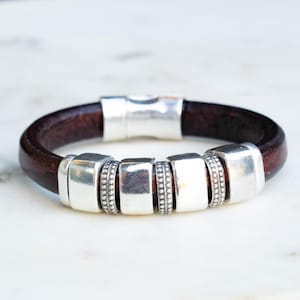 May include: A dark brown leather bracelet with silver-toned rectangular and beaded accents. The bracelet has a magnetic clasp. The design is simple and elegant, suitable for everyday wear.