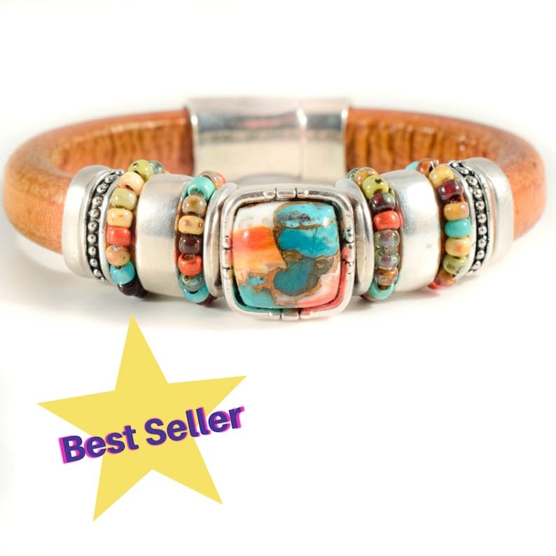 May include: A leather bracelet with a central square turquoise stone, framed by a silver setting. The bracelet features colorful beaded accents in shades of red, green, and blue. The band is a light brown color.