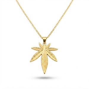 May include: A gold-toned necklace featuring a pendant shaped like a seven-pointed cannabis leaf. The pendant has a textured, etched surface detail on each leaf segment and hangs from a delicate, matching gold-toned metal chain link necklace.