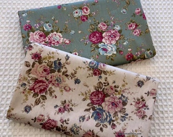 May include: Two floral fabric swatches. One is a light green fabric with a pink and blue floral pattern. The other is a beige fabric with a pink and blue floral pattern. The fabric is folded and the text "fabricmadeeasy.com" is visible on the beige fabric.