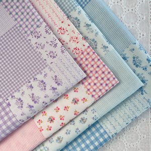 May include: A selection of fabric swatches in pastel shades. The fabrics display floral, gingham, and striped designs in lavender, pink, and blue. The fabrics are arranged diagonally, showcasing the different patterns.