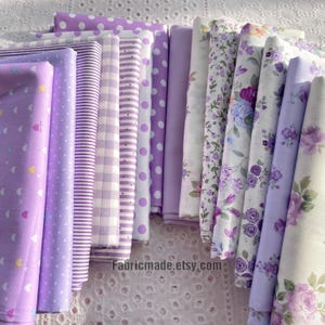 Può includere: Una collezione di tessuti arrotolati in varie tonalità di viola e bianco. I motivi includono pois, righe, quadretti e disegni floreali. Il tessuto è disposto verticalmente, mostrando una varietà di trame e stampe. Il nome del negozio Etsy "Fabricmade.etsy.com" è visibile.
