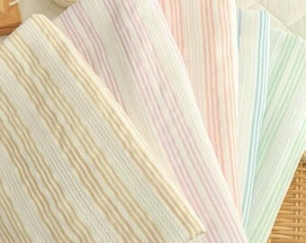 May include: A collection of striped fabric samples in various pastel colors, including beige, pink, and green. The fabrics are arranged in a fan shape, showcasing their different hues and textures. A ball of white yarn is also visible.