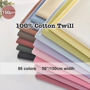 Könnte beinhalten: Ein Stapel aus 100 % Baumwoll-Twill-Stoff in verschiedenen Farben, darunter Rosa, Lila und Blau. Der Stoff ist 150 cm breit und 150 g/m². Der Text im Bild lautet "86 Farben".
