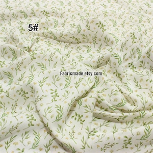 May include: White fabric with a green and yellow floral pattern. The fabric has a subtle texture and a soft, flowing drape. The pattern features small, delicate leaves and flowers. The fabric is ideal for crafting, quilting, and sewing projects.