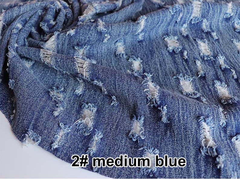 May include: Close-up of a medium blue denim fabric with distressed holes and frayed edges. The fabric is textured and has a worn look. The text "2# medium blue" is visible in the bottom right corner of the image.