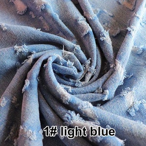 May include: Close-up of light blue distressed denim fabric with frayed edges. The fabric is folded and twisted, showing the texture and detail of the distressed look. The text "1# light blue" is visible in the lower right corner of the image.