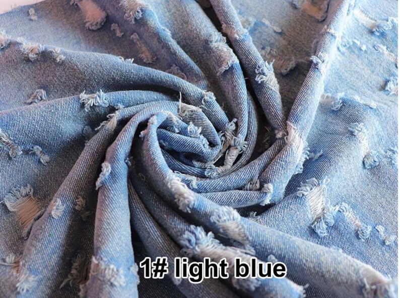 May include: Close-up of light blue distressed denim fabric with frayed edges. The fabric is folded and twisted, showing the texture and detail of the distressed look. The text "1# light blue" is visible in the lower right corner of the image.
