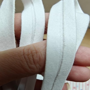 May include: Close-up of white bias tape, a fabric strip folded and pressed to create a finished edge. The tape is made of a soft, woven material. The image shows the tape in a close-up view, highlighting its texture and construction.
