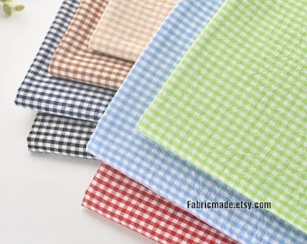May include: A stack of gingham fabric in various colors, including red, blue, green, tan, brown, and black. The fabric is arranged in a layered pattern, with the red fabric at the bottom. The website address Fabricmade.etsy.com is visible on the red fabric.