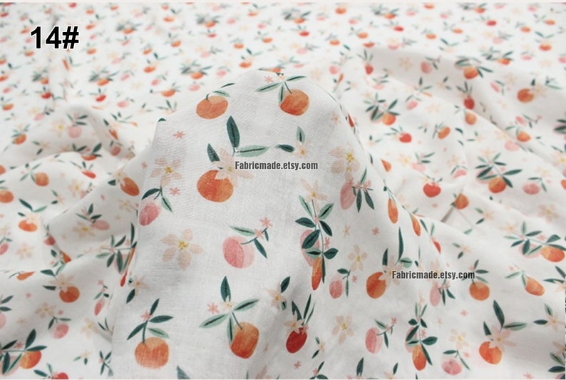 Peut inclure: Tissu en coton blanc avec un motif r&eacute;p&eacute;t&eacute; de fruits orange, de feuilles vertes et de fleurs roses. Le tissu est pli&eacute; et le texte "14#" est visible dans le coin sup&eacute;rieur gauche.