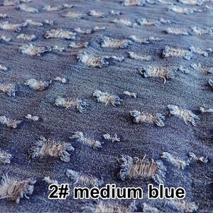 May include: Close-up of a medium blue denim fabric with distressed holes. The fabric has a rough texture and a faded appearance. The text "2# medium blue" is visible in the bottom right corner of the image.
