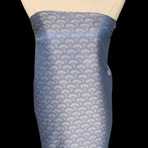 May include: A light blue fabric with a white and light blue patterned design. The pattern is a repeating design of overlapping fan shapes.