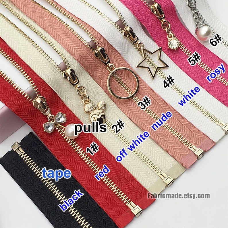 May include: Assortment of zipper tapes with different colors and pull charms. The colors include black, red, off white, nude, white, and rosy. The charms include a star, a circle, a Mickey Mouse head, a bow with a pearl, and a pearl.