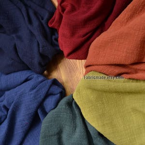 Può includere: Una collezione di sei campioni di tessuto in vari colori, tra cui blu navy, blu scuro, rosso, arancione, verde e verde oliva. Il tessuto è un lino naturale con una trama tessuta. I campioni sono disposti in un cerchio su una superficie di legno. Il testo "Fabricmade.etsy.com" è visibile nell'angolo in basso a destra dell'immagine.