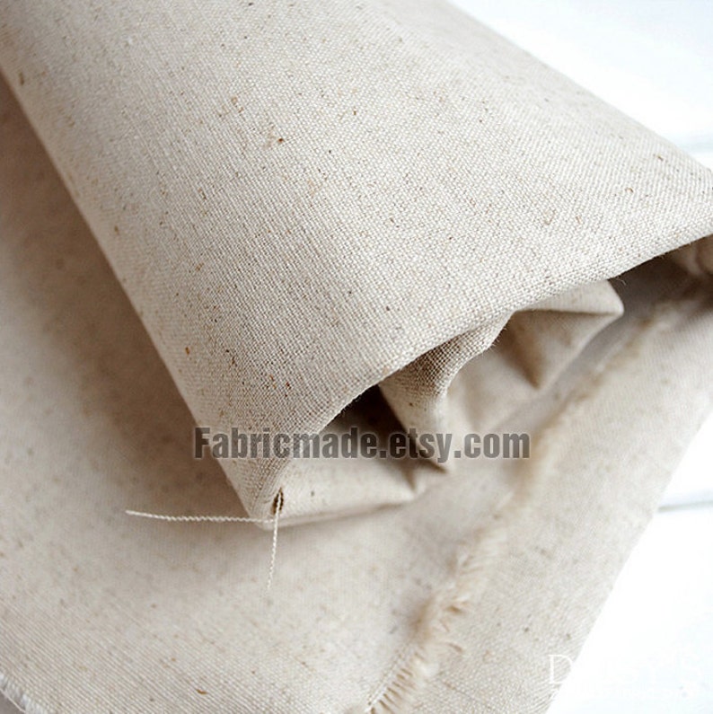 May include: Close-up of a natural beige linen fabric with a slightly textured surface. The fabric is rolled up and has a raw edge.