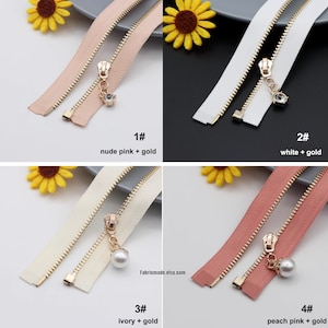 May include: Four different zipper pulls with gold metal zippers and different colored zipper tapes. The zipper pulls are decorated with a crystal, a pearl, and a pearl. The zipper tapes are nude pink, white, ivory, and peach pink.
