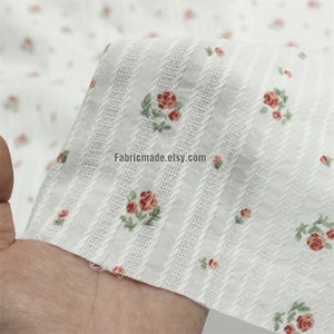 May include: White cotton fabric with a small rose print and vertical textured stripes. The fabric is shown being held in a hand. The text "Fabricmade.etsy.com" is visible in the image.