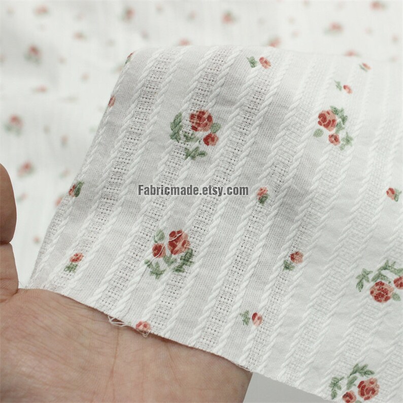 May include: White cotton fabric with a small rose print and vertical textured stripes. The fabric is shown being held in a hand. The text "Fabricmade.etsy.com" is visible in the image.