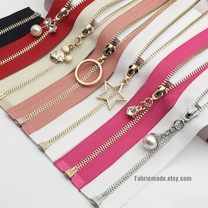 May include: Assortment of zipper tapes with different colors and decorative zipper pulls. The pulls include a star, a circle, a Mickey Mouse head, a rhinestone, and a pearl.