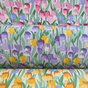 May include: A close-up of a fabric with a repeating pattern of purple, yellow, and white tulips on a light purple background. The fabric is folded in thirds, showing the pattern from different angles.