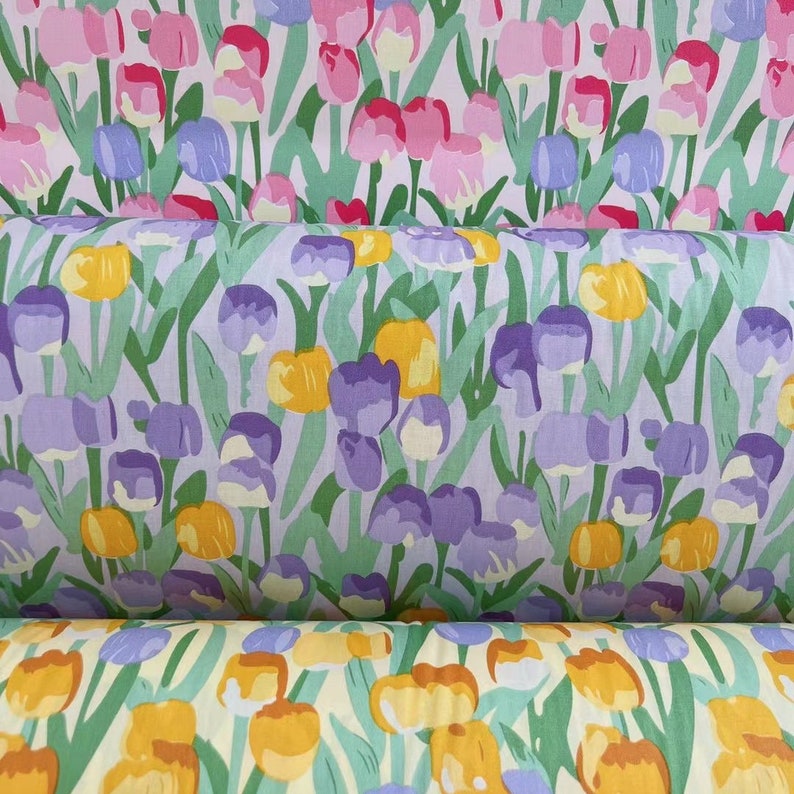 May include: A close-up of a fabric with a repeating pattern of purple, yellow, and white tulips on a light purple background. The fabric is folded in thirds, showing the pattern from different angles.