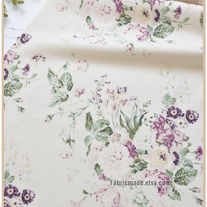 Puede incluir: Tela blanca con estampado floral con flores rosas, moradas y verdes. La tela tiene una textura sutil y una sensaci&oacute;n suave y vintage.