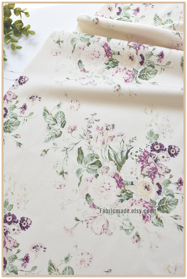 Puede incluir: Tela blanca con estampado floral con flores rosas, moradas y verdes. La tela tiene una textura sutil y una sensaci&oacute;n suave y vintage.