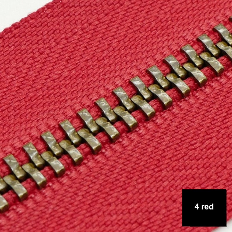 May include: Close-up of a red zipper with a brass zipper pull. The zipper is made of a woven fabric and has a smooth finish. The zipper pull is made of metal and has a textured finish. The zipper is labeled "4 red".