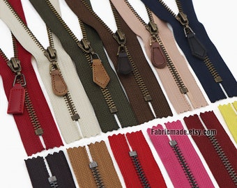 May include: Assortment of 12 zipper tapes in various colors, including red, brown, black, beige, green, pink, and blue. The zippers have brass sliders and are arranged in two rows. The text "Fabricmade.etsy.com" is visible in the bottom right corner of the image.