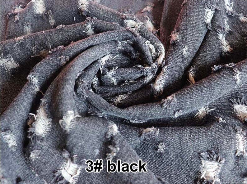 May include: Close-up of a dark gray denim fabric with a distressed, ripped look. The fabric is folded and textured, showing the frayed edges of the rips. The text "3# black" is visible in the lower right corner of the image.
