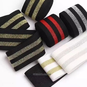 May include: Assortment of black elastic trim with two stripes of gold, silver, and red glitter. The trim is rolled up and arranged on a white surface.