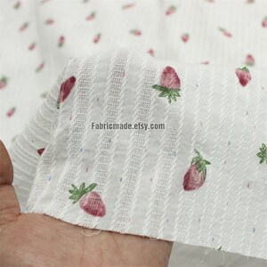 May include: White cotton fabric with a striped pattern and a small pink strawberry print. The fabric is textured and has a subtle sheen. The text "Fabricmade.etsy.com" is printed on the fabric.