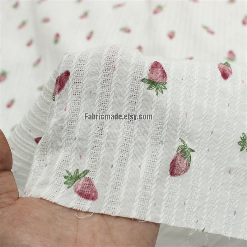 May include: White cotton fabric with a striped pattern and a small pink strawberry print. The fabric is textured and has a subtle sheen. The text "Fabricmade.etsy.com" is printed on the fabric.