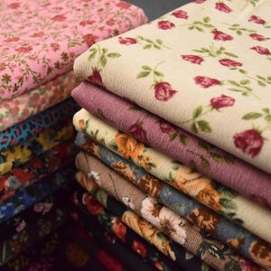 Peut inclure: Une pile de tissus à motifs floraux de différentes couleurs. Les tissus présentent des motifs de roses et d'autres fleurs dans des tons de rose, crème, violet, orange, bleu et marron. Le tissu a une texture en velours côtelé.