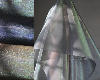 May include: Iridescent fabric in shades of silver, blue, and gold. The fabric is draped over a form, showcasing its shimmering qualities. The image also shows rolls of the fabric, highlighting its texture and color variations. The website address fabricmade.etsy.com is visible.