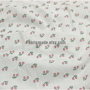 May include: White fabric with a repeating pattern of pink cherries with green stems and leaves. The fabric has a subtle striped texture.