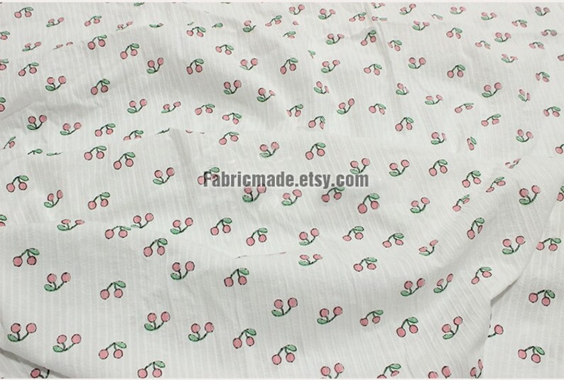 May include: White fabric with a repeating pattern of pink cherries with green stems and leaves. The fabric has a subtle striped texture.