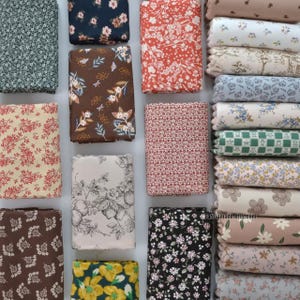 May include: A selection of folded fabric squares featuring floral patterns in diverse colours. Designs include small and large flowers in red, blue, brown, and green. A stack of rolled fabric with floral patterns is also visible.