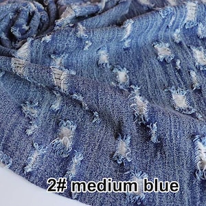 May include: Close-up of a blue denim fabric with distressed holes. The fabric is folded and has a rough texture. The text "2# medium blue" is visible in the bottom right corner.
