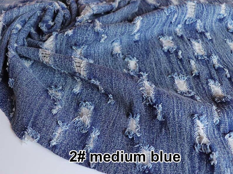 May include: Close-up of a blue denim fabric with distressed holes. The fabric is folded and has a rough texture. The text "2# medium blue" is visible in the bottom right corner.