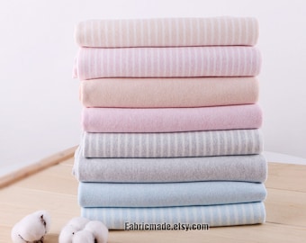 May include: A stack of folded fabric in various pastel colors, including pink, beige, gray, and blue. Some fabrics have white stripes. Two cotton buds are on a wooden surface. The website address fabricmade.etsy.com is visible.
