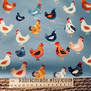 May include: A light blue fabric featuring a repeating pattern of chickens in various colors including white, orange, black, and blue. A wooden ruler is positioned at the bottom, showing measurements in inches and centimeters for scale.