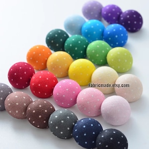 Puede incluir: Un surtido arcoíris de botones cubiertos de tela con lunares blancos. Los botones están dispuestos en diagonal, con el botón más grande en la parte superior y el botón más pequeño en la parte inferior.