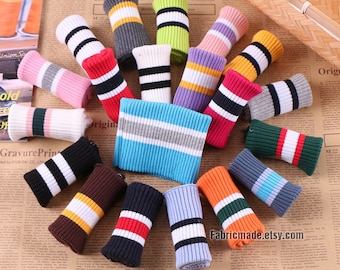 Op de afbeelding: Een assortiment van kleurrijke gebreide stofmanchetten met gestreepte patronen. De manchetten zijn opgerold en in een cirkel gerangschikt op een bruin en wit gepatroneerd oppervlak. De tekst "Fabricmade.etsy.com" is zichtbaar in de rechterbenedenhoek van de afbeelding.