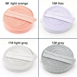 May include: Four spools of elastic ribbon in light orange, lilac, light gray, and gray. Each spool is labeled with a number and color name. The elastic is folded over and appears to be ready for use in sewing or crafting projects.